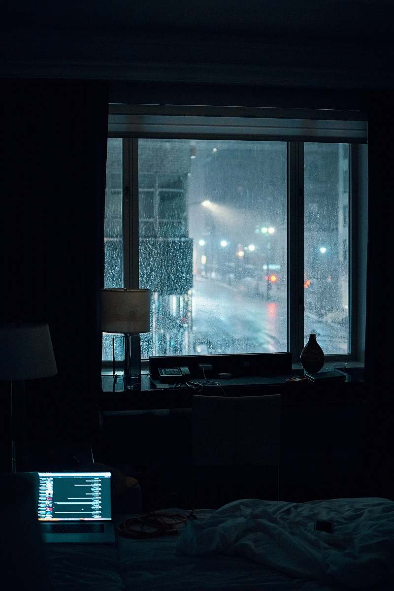 united states laptop computer left turned-on on bed inside room during rainy night moody
